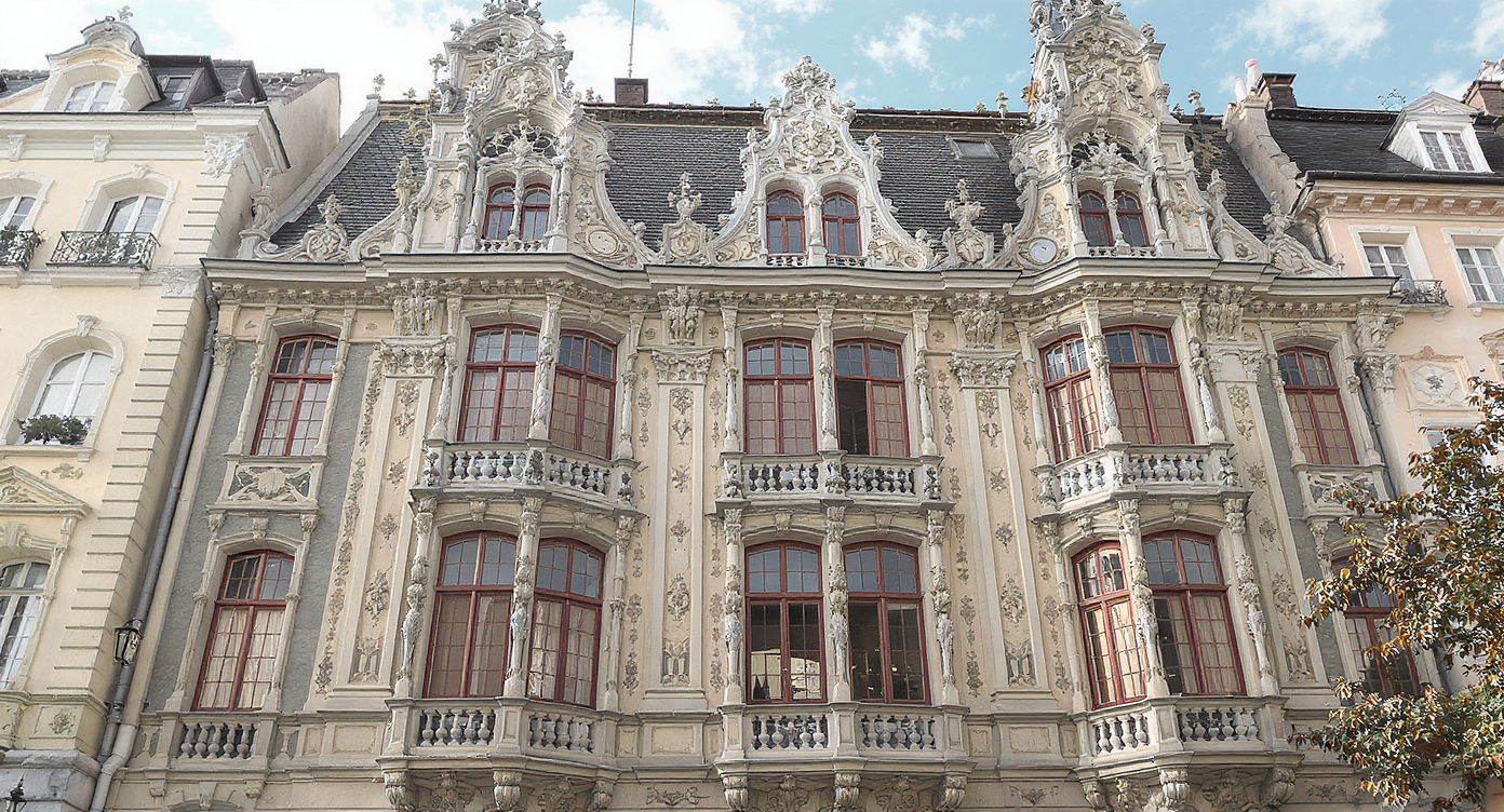 Ein prächtiges historisches Gebäude mit reich verziertem Fassadenwerk, mehreren Stockwerken, Balkonen und roten Fensterrahmen.